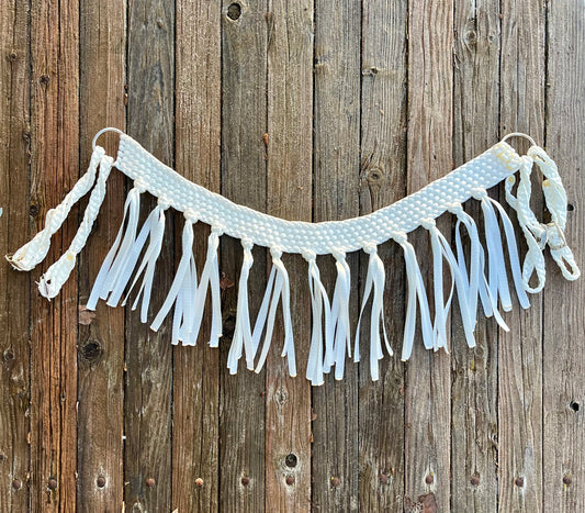 A white mule tape horse tripping collar with fringe and metal hardware, displayed against a wooden background.