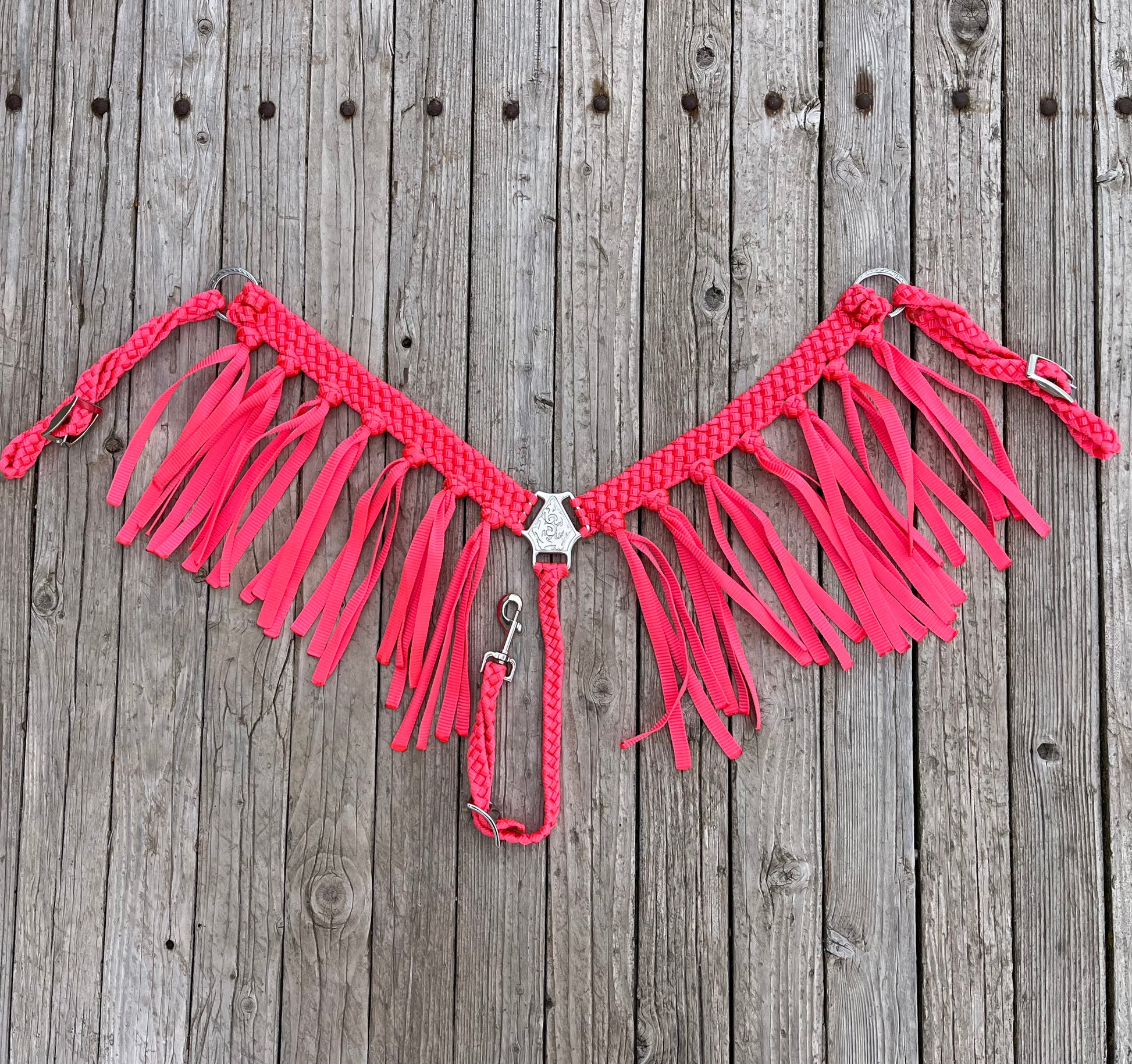 A neon pink mule tape breast collar with fringe and Jeremiah Watts hardware  laid out on a wooden surface.